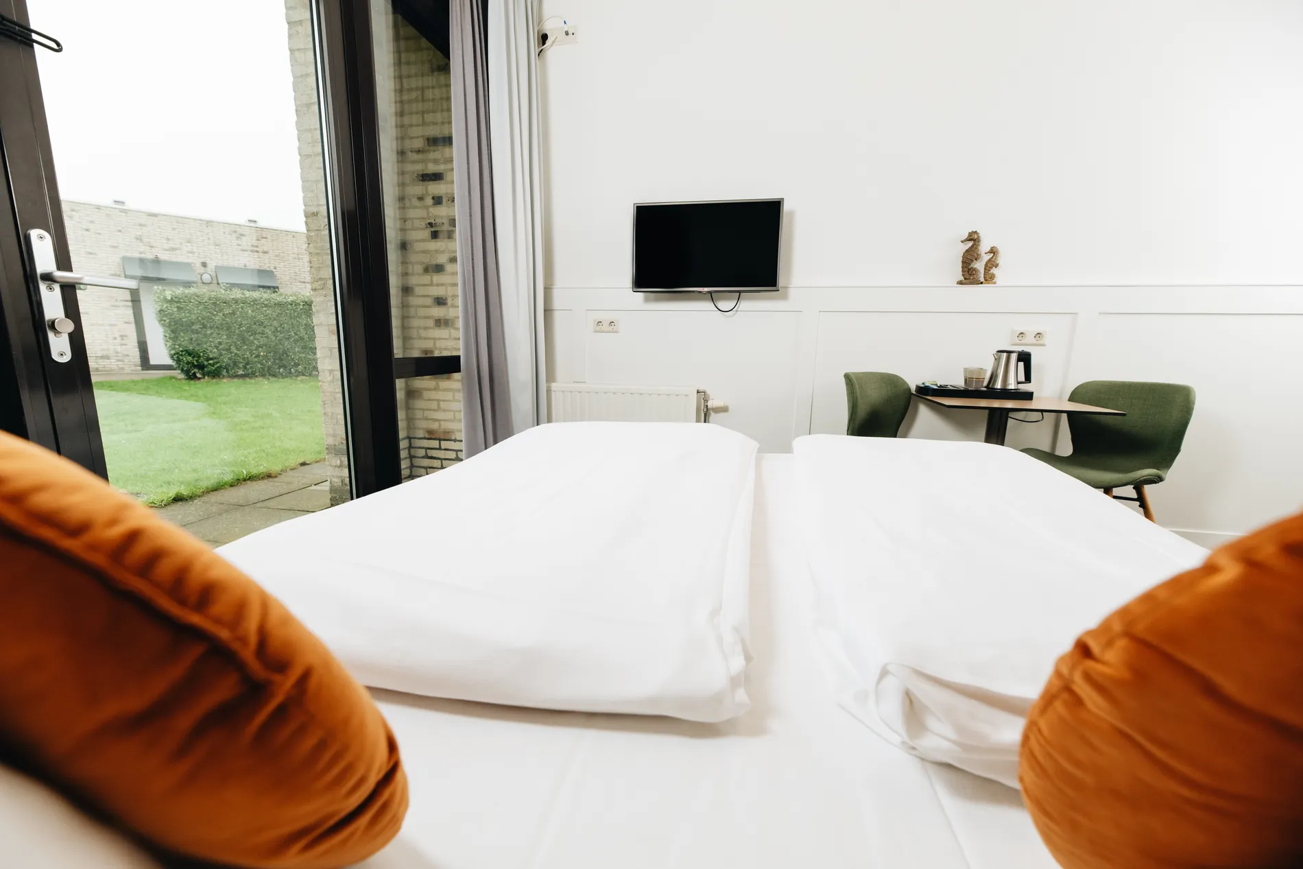 Modern interieur van een hotelkamer met een aan de wand gemonteerde tv, een gezellig zitje met groene stoelen en koffiefaciliteiten.